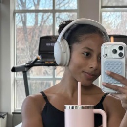 a woman taking a picture at a fitness center holding a water bottle and wearing headphones